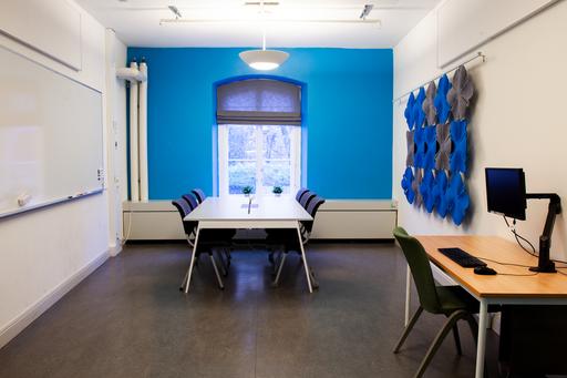 Grupprum med whiteboard, bord, stolar och datorarbetsplats.